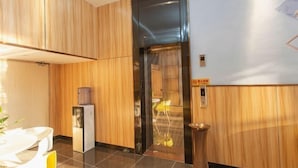 Un vestíbulo moderno con paneles de madera, un dispensador de agua, un ascensor de vidrio y un cubo de basura.