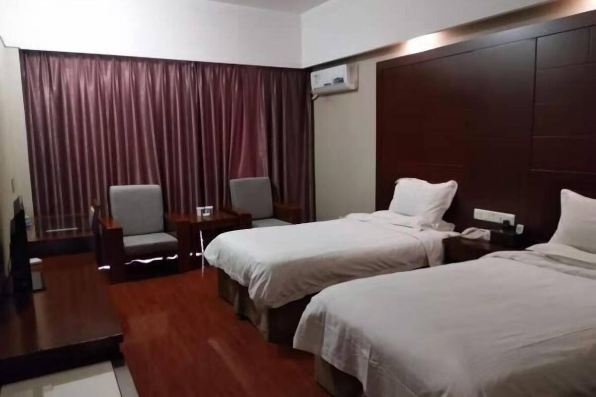 A hotel room with two beds, a desk, a chair, and a large window with curtains.