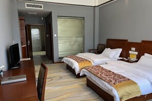Ein Hotelzimmer mit zwei Betten, einem Schreibtisch, einem Fernseher und einem großen Fenster mit Jalousien.