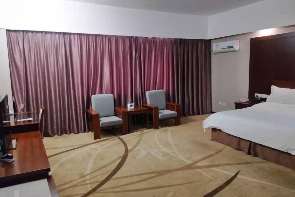 A hotel room with a large bed, two armchairs, a desk, and a carpeted floor.