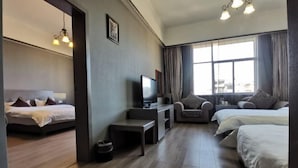 Habitación de hotel con dos camas, un escritorio con televisor, una silla y un ventanal con cortinas.