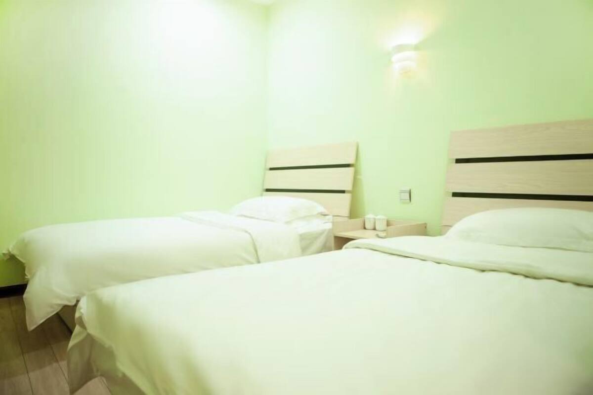 A hotel room with two beds, a nightstand, and a wall-mounted light.