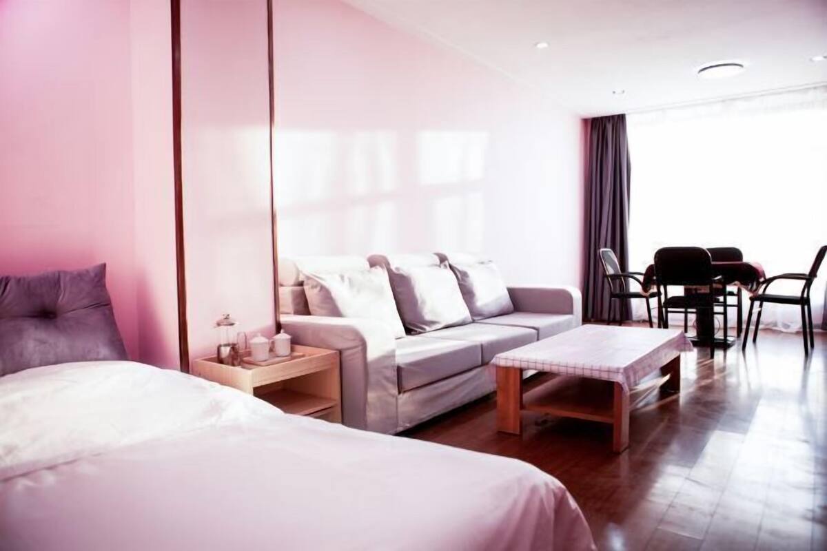 A modern hotel room with a large bed, a sofa, a small table, and a dining area with chairs.