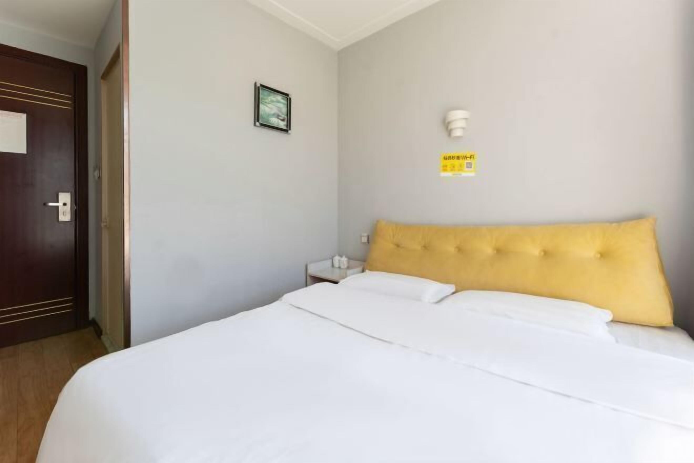 A hotel room with a large bed, a wooden door, a small bedside table, and a wall-mounted light fixture.