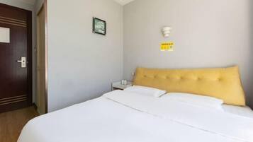 A hotel room with a large bed, a wooden door, a small bedside table, and a wall-mounted light fixture.