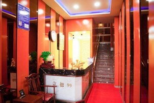 A hotel reception area with a reception desk, chairs, a staircase, and a red carpet.