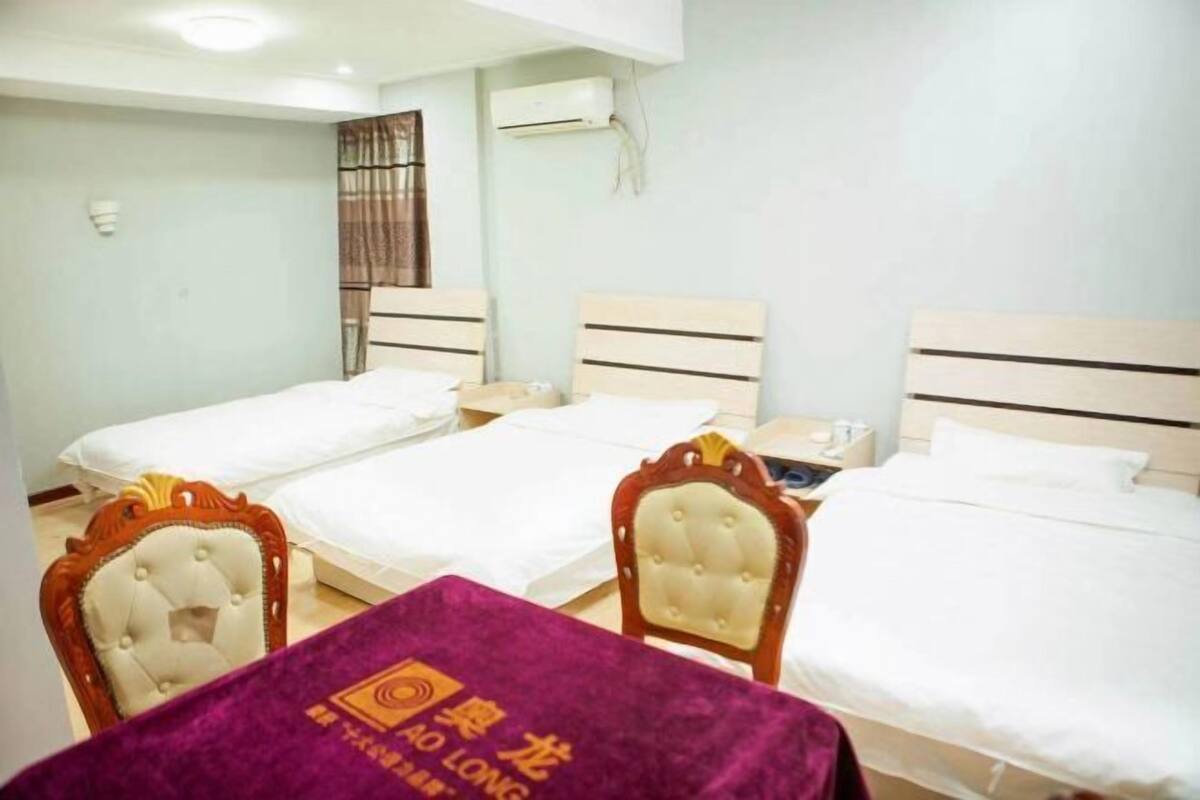 A hotel room with three beds, a table with a purple tablecloth, and a chair.