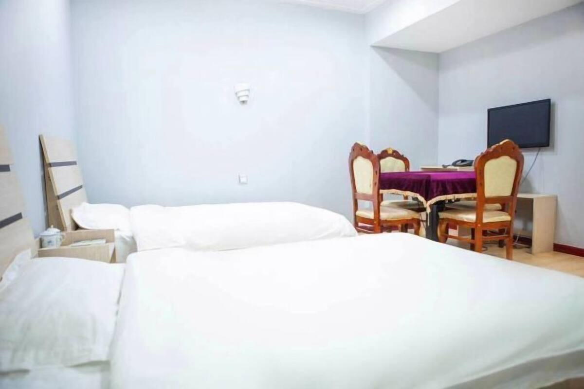 A hotel room with two single beds, a desk with a chair, a television, and a small table.