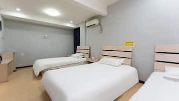 Habitación de hotel con dos camas individuales, un escritorio, una silla, un equipo de aire acondicionado y un estante pequeño.