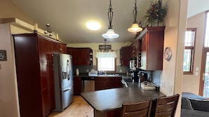A kitchen with wooden cabinets, a central island with chairs, a refrigerator, and a microwave. - Deadwood & Sturgis 5 bedroom next to golf course (Sturgis)