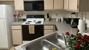 A kitchen with light wooden cabinets, a white refrigerator, a black microwave, a stove, and a sink. - Botanical Retreat: King Comfort & Poolside Peace (Gainesville)