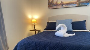 A neatly made bed with a dark blue quilt, two pillows, a swan-shaped towel, and a lamp on a bedside table. - Botanical Retreat: King Comfort & Poolside Peace (Gainesville)