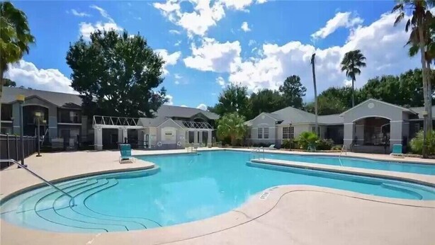A swimming pool with a clear blue water feature, surrounded by a concrete deck and palm trees. - Botanical Retreat: King Comfort & Poolside Peace (Gainesville)