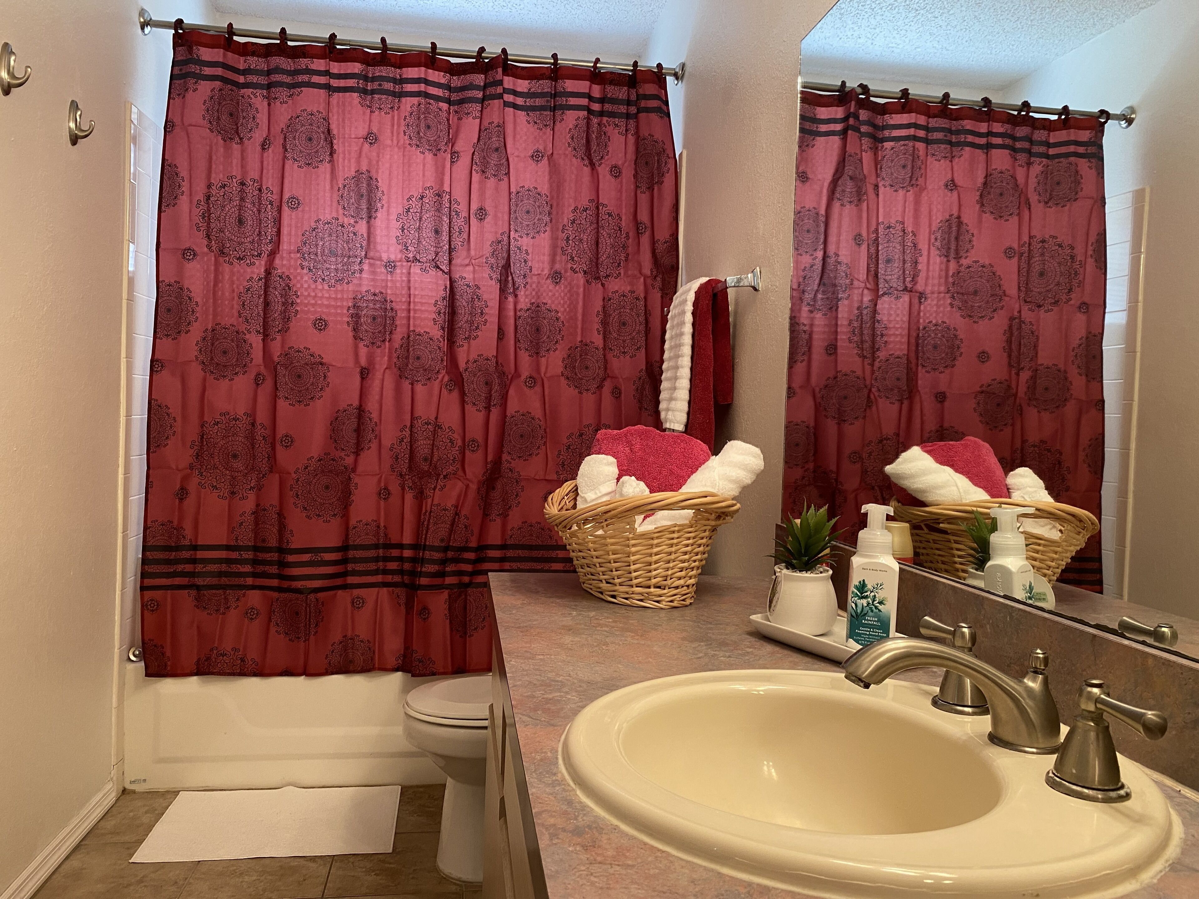 A bathroom with a toilet, sink, and a shower curtain with a floral pattern. There are baskets with towels and toiletries on the counter.
