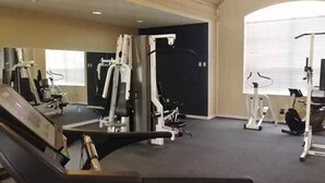 A gym with various exercise machines, a mirrored wall, and a large window. - Botanical Retreat: King Comfort & Poolside Peace (Gainesville)