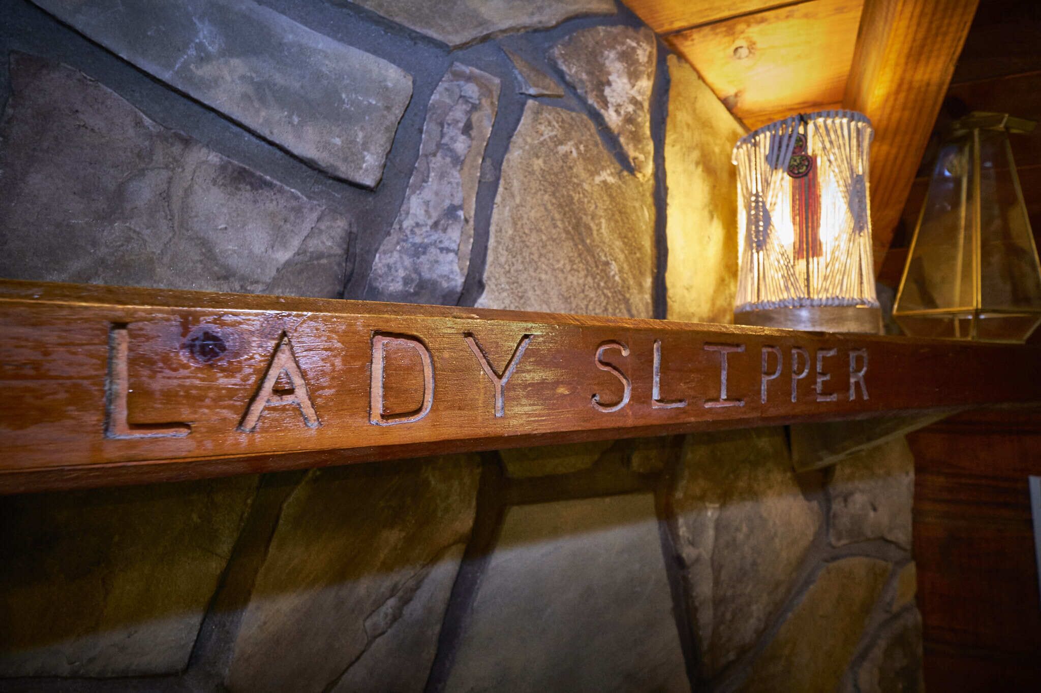 Una estantería de madera con la inscripción 'LADY SLIPPER' sobre un muro de piedra.