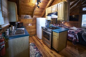 Une cuisine de taille réduite, dotée de meubles en bois, d’un réfrigérateur, d’un four à micro-ondes et d’un four traditionnel.