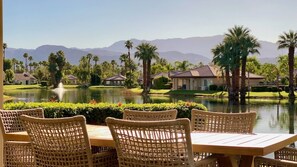 A view of a golf course with a pond, palm trees, and houses in the background. - Aqua Vista | Inspiring Views, 2 Suites & Spacious Patio – a Greenday property (Rancho Mirage)