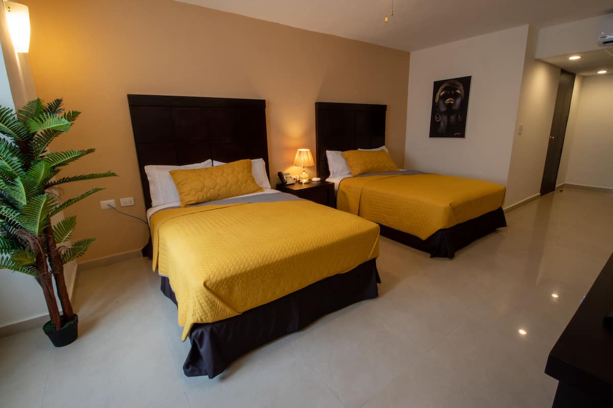 A hotel room with two beds, a nightstand with a lamp, a potted plant, and a painting on the wall.