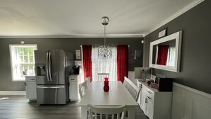 A modern kitchen with a stainless steel refrigerator, a dining table with white chairs, and a chandelier.