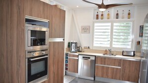 A modern kitchen with wooden cabinetry, stainless steel appliances, and a large window with blinds.