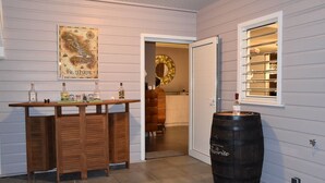 A wooden bar with bottles and a large black barrel in a room with white walls and a window.