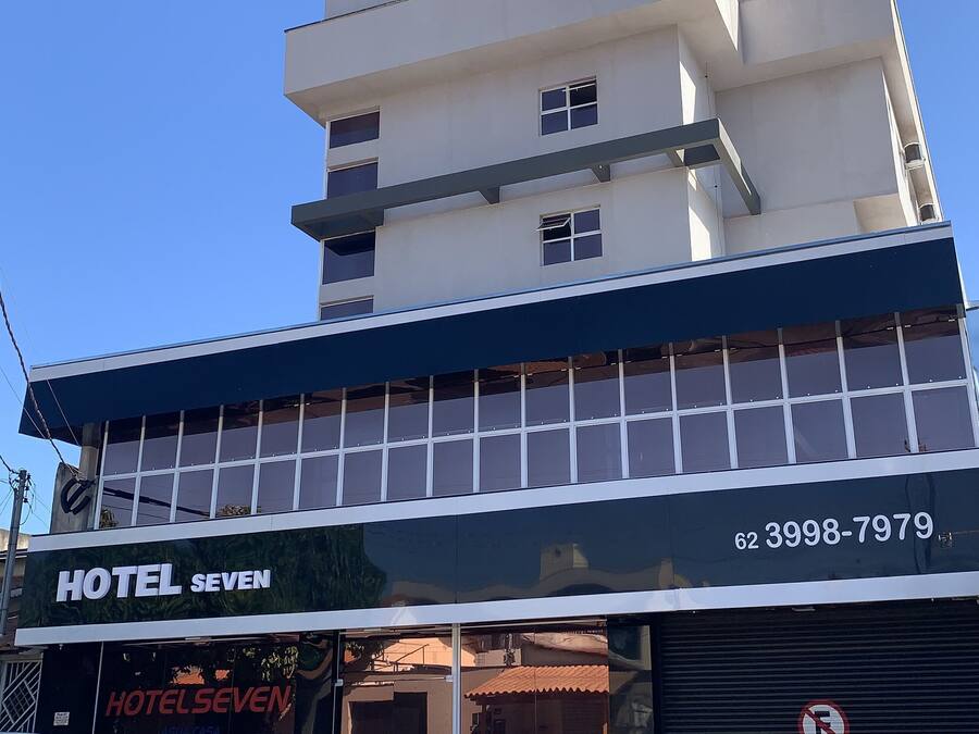 Um hotel com uma placa grande 'HOTEL' no topo, um número de contato '62 3998-7979' na fachada, e uma placa indicando 'GARAGEM'.