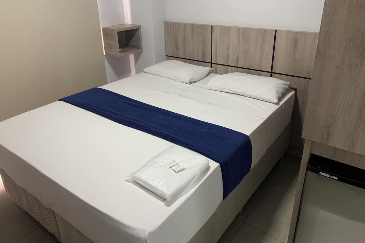 A neatly made bed with white bedding and a blue accent, a wooden headboard, and a small bedside table with a white pillow.