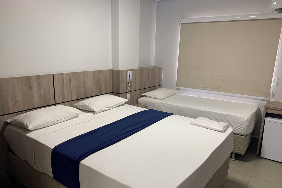 A hotel room with two beds, a small desk, a telephone, and a window with a blind.