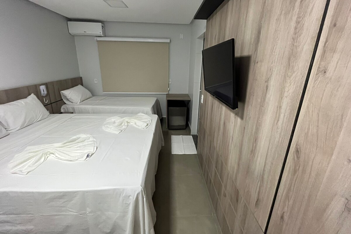 A hotel room with two beds, a TV mounted on the wall, and a wooden wardrobe.