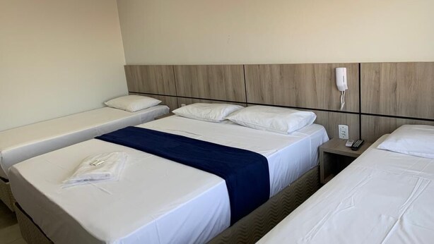 A hotel room with three beds, a wooden headboard, a bedside table with a phone, and a wall socket. - HOTEL SEVEN (Goiânia)