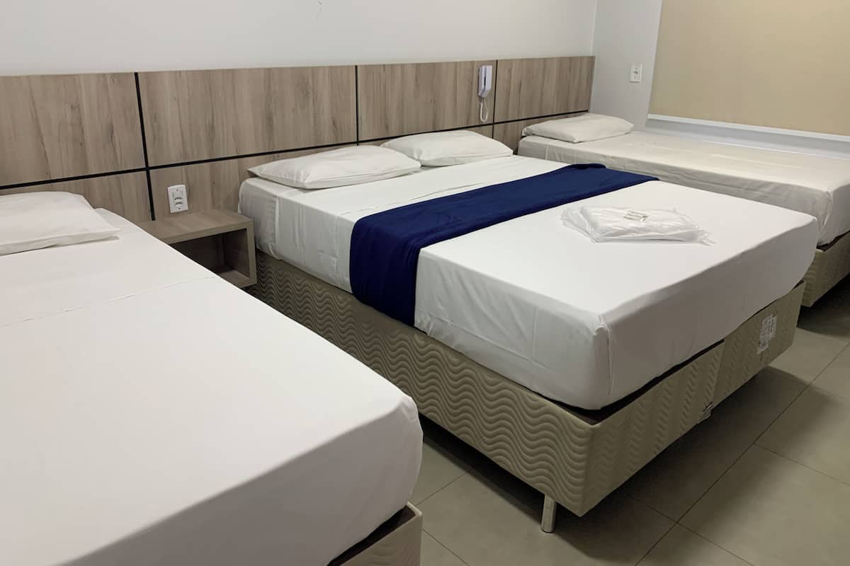 A hotel room with two single beds and a larger bed with a blue blanket.