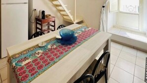 Una cocina compacta con una mesa de madera, sillas, un refrigerador y una escalera que sube a un nivel superior.