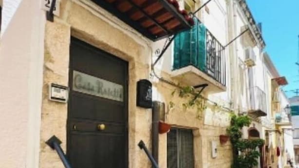 Un edificio con fachada de piedra, una puerta oscura y unos pequeños escalones de piedra que conducen a un balcón.