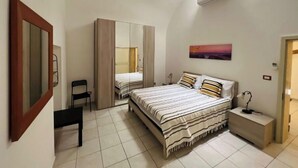 Un dormitorio con cama, mesita de noche, armario, silla, espejo y un cuadro en la pared.
