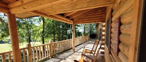 A wooden deck with a railing, a wooden chair, and a grill area.