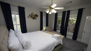 Ein Schlafzimmer mit einem großen Bett, einem Sessel, einem Deckenventilator und mehreren Fenstern.