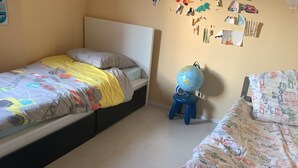 A bedroom with two beds, one with a colorful bedspread and the other with a patterned one. There is a globe on a stool next to one bed. - Paris 12th (Paris)