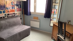 A room with a grey sofa, a wooden desk with a chair, a radiator, and a window with curtains. - Paris 12th (Paris)