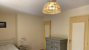 Een slaapkamer met een bed, een kaptafel, een nachtkastje, een lamp en een deur.
