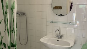 Een badkamer met een witte wastafel, een glazen plank, een spiegel en een douche met een douchegordijn met bamboedesign.