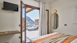 Une chambre d’hôtel comprenant un lit, une télévision, une table de chevet, un miroir et une vue sur un balcon donnant sur une piscine et des montagnes.