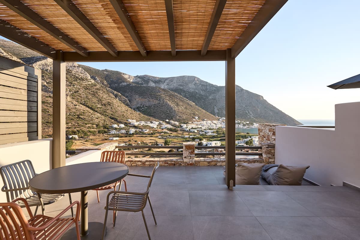 Un espace extérieur abrité, doté d’une table et de chaises, qui offre une vue sur un paysage montagneux parsemé de bâtiments blancs.