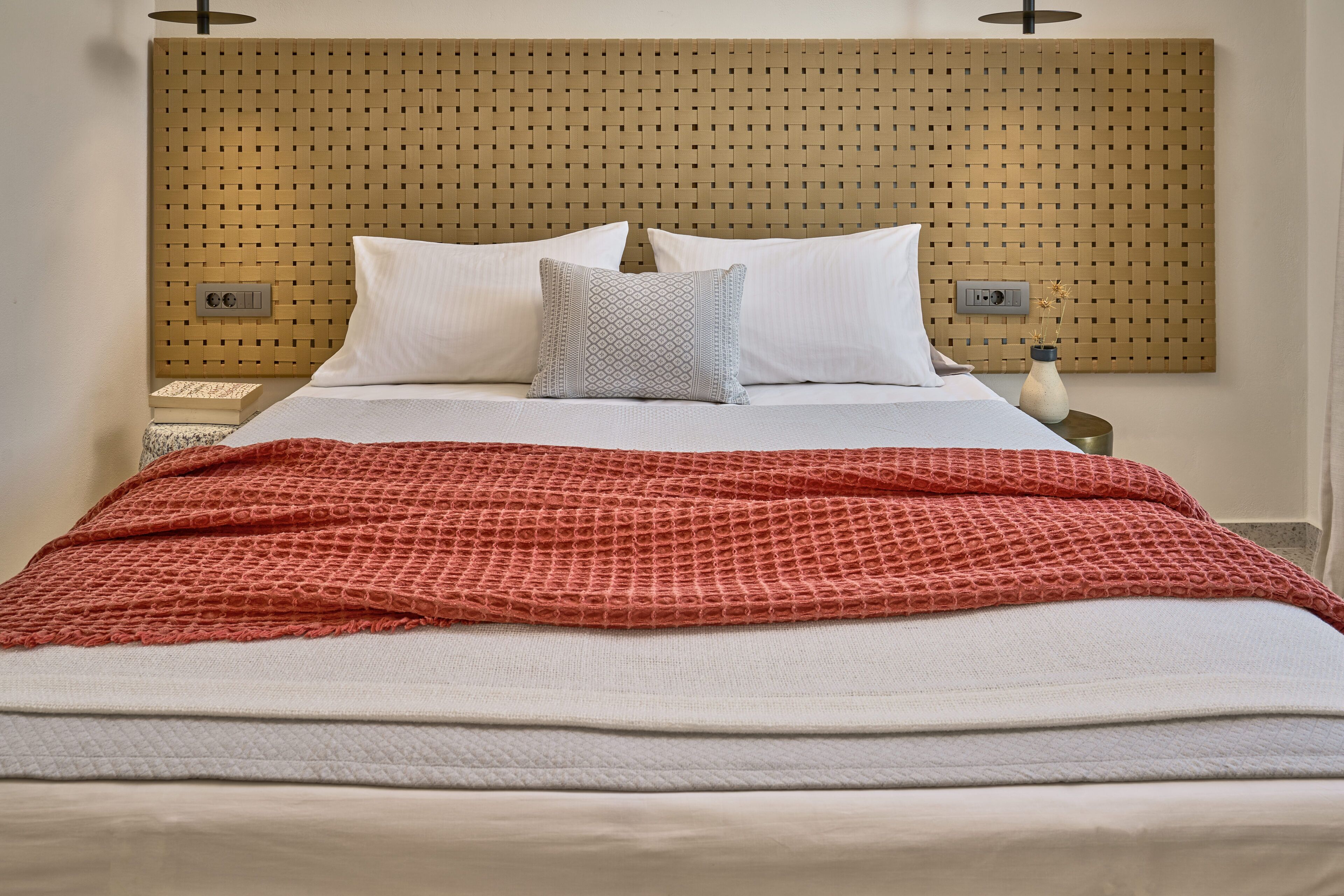 A neatly made bed with white and red bedding, a woven headboard, and bedside tables with lamps.
