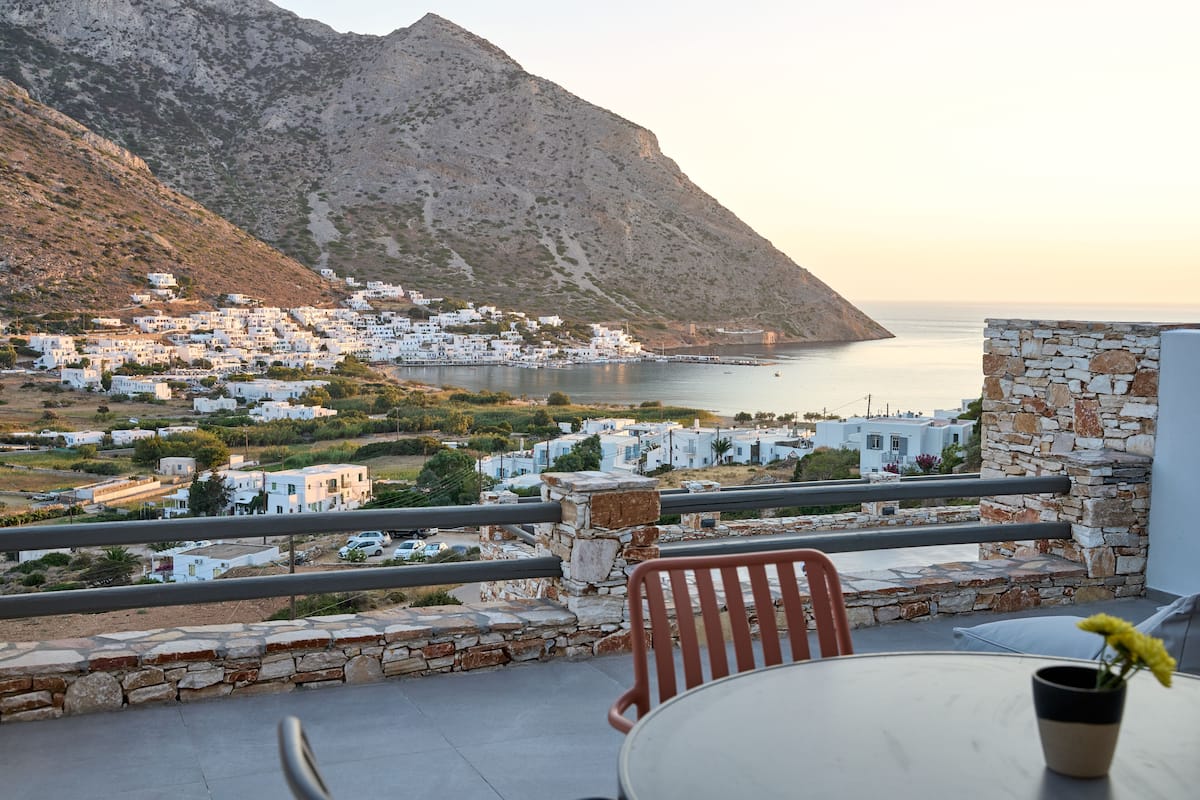 Une terrasse avec une table et des chaises donnant sur un village côtier aux bâtiments blancs, avec une montagne en arrière-plan.