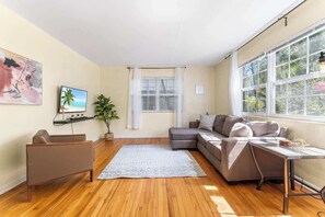 A modern living room with a sofa, a coffee table, a TV, a plant, and a window with curtains.