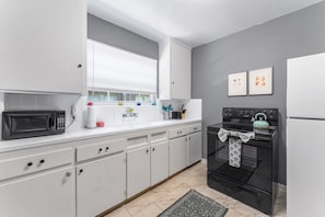 A modern kitchen with white cabinets, a black microwave, a stove, and a window with blinds.