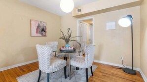 A dining area with a round table, four chairs, a floor lamp, a plant, and a painting on the wall. - Eclectic Escape #2 - Team Joseph Ellen (Jacksonville)