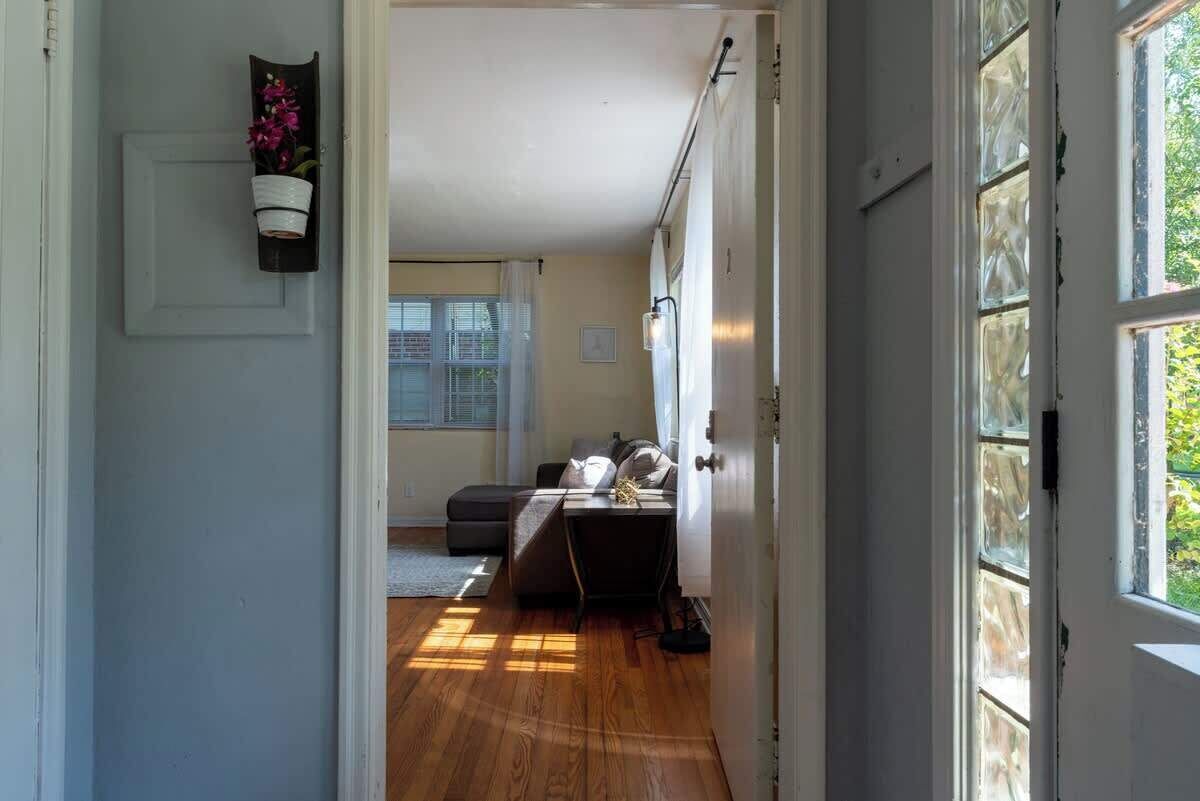A hallway leading to a bedroom with a bed, a bedside table, and a window.