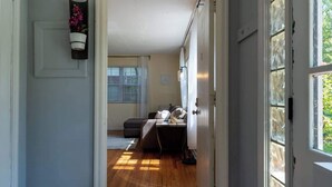 A hallway leading to a bedroom with a bed, a bedside table, and a window. - Eclectic Escape #2 - Team Joseph Ellen (Jacksonville)